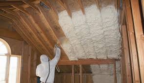 A technician installs spray foam installation on a ceiling between joists.