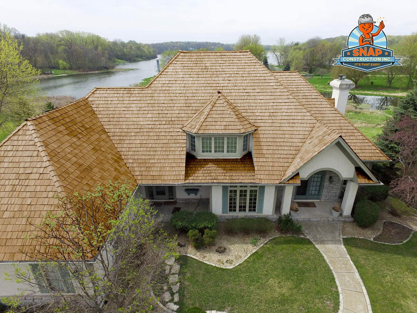A large home with wood shake roofing has a lake in the background.