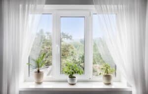 Window with white tulle and potted plants on windowsill.