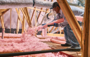 Man in an attic using machine to blow fiberglass insulation