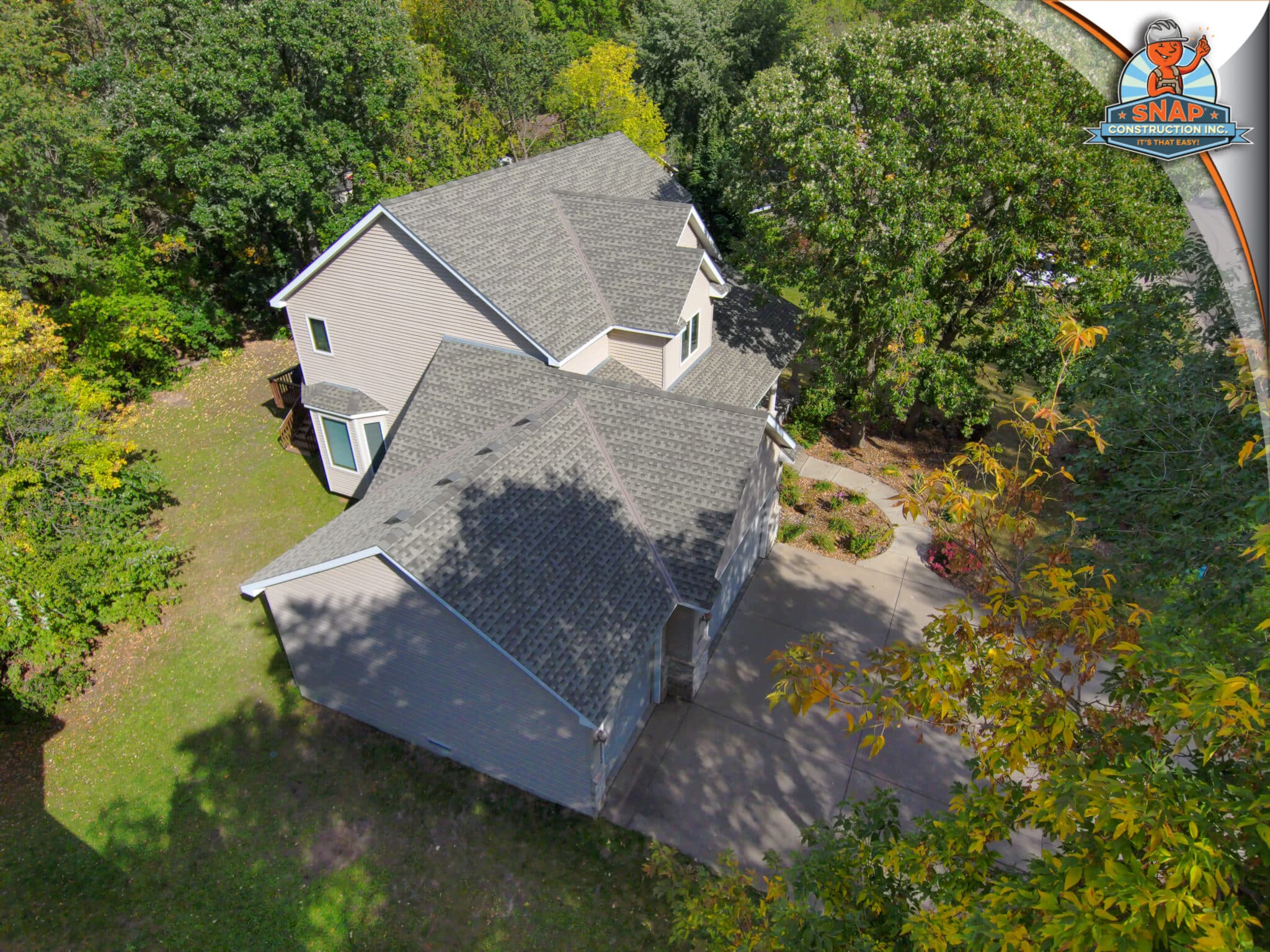 Aerial view of asphalt shingle roof installation on a suburban home in Bloomington MN by Snap Construction, surrounded by mature trees