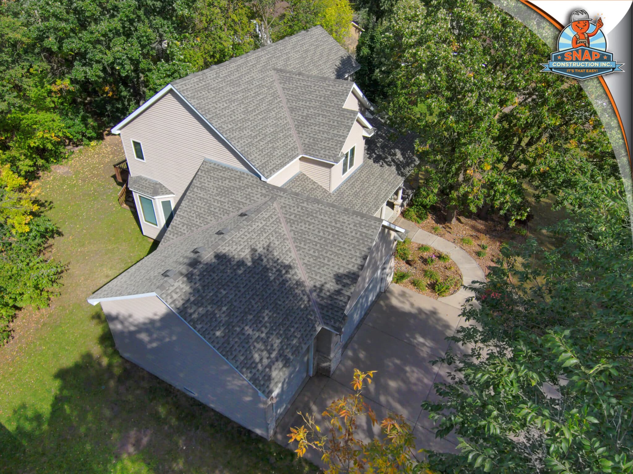 Aerial view of a Bloomington MN home with new asphalt shingles by Snap Construction, roof replacement contractor in Bloomington, amid trees
