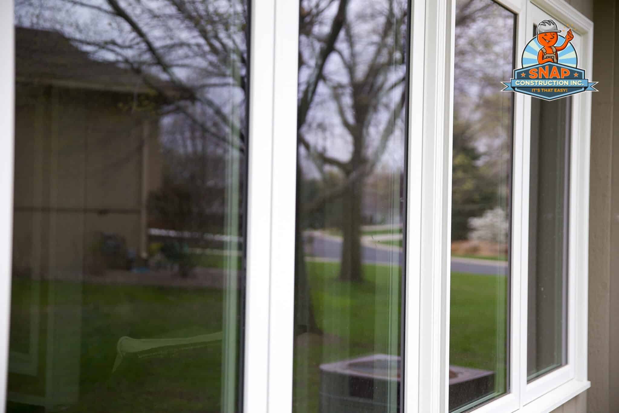 Close-up of white-framed energy efficient windows by Snap Construction in Bloomington MN, reflecting trees and a suburban lawn