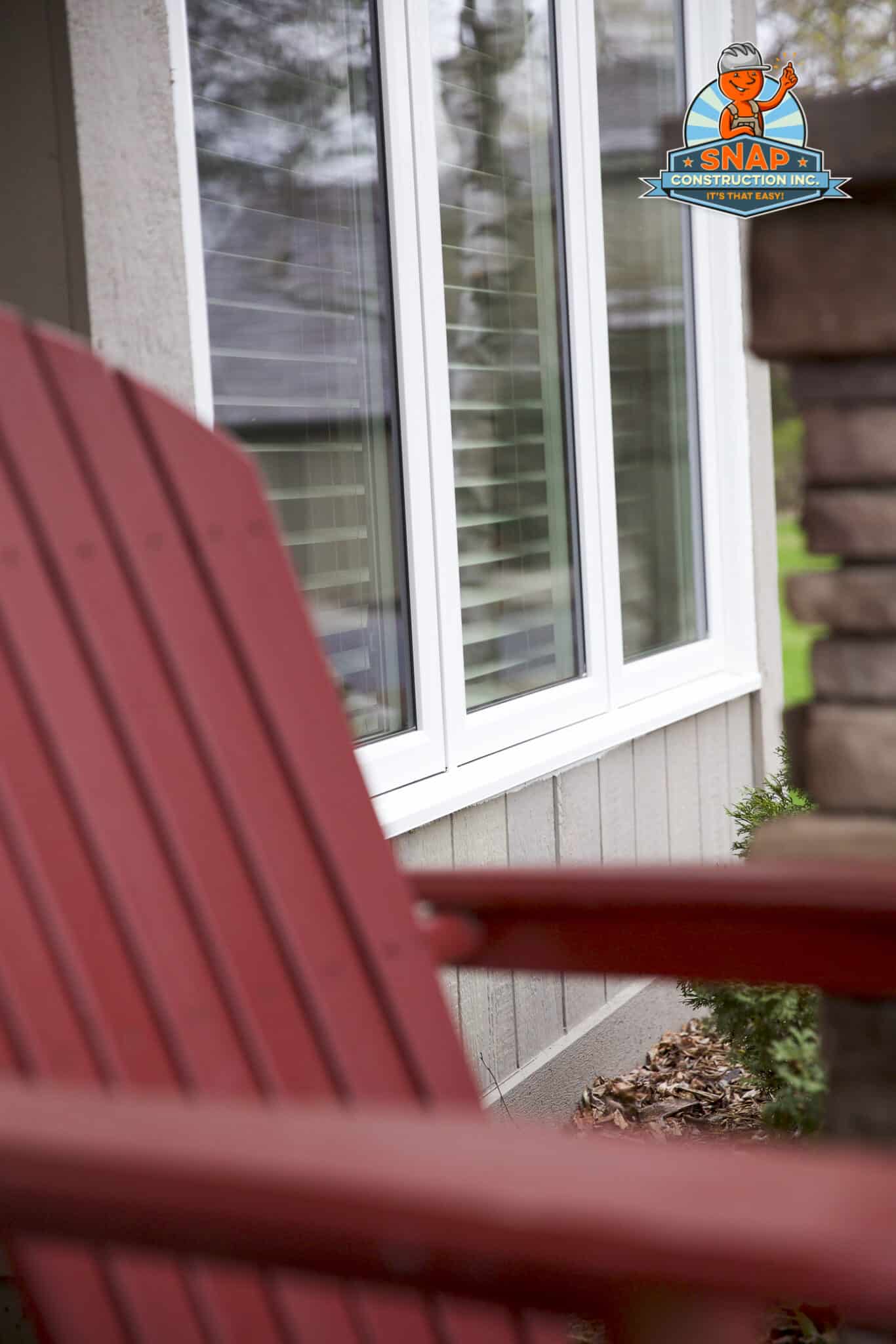 Snap Construction window contractor in Bloomington MN installs white framed house windows beside a red Adirondack chair and stone column
