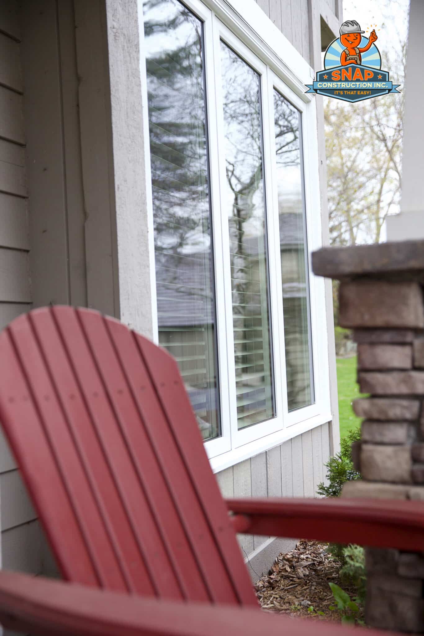 Snap Construction replacement windows in Bloomington MN, white-framed windows on gray siding beside a porch with red Adirondack chair