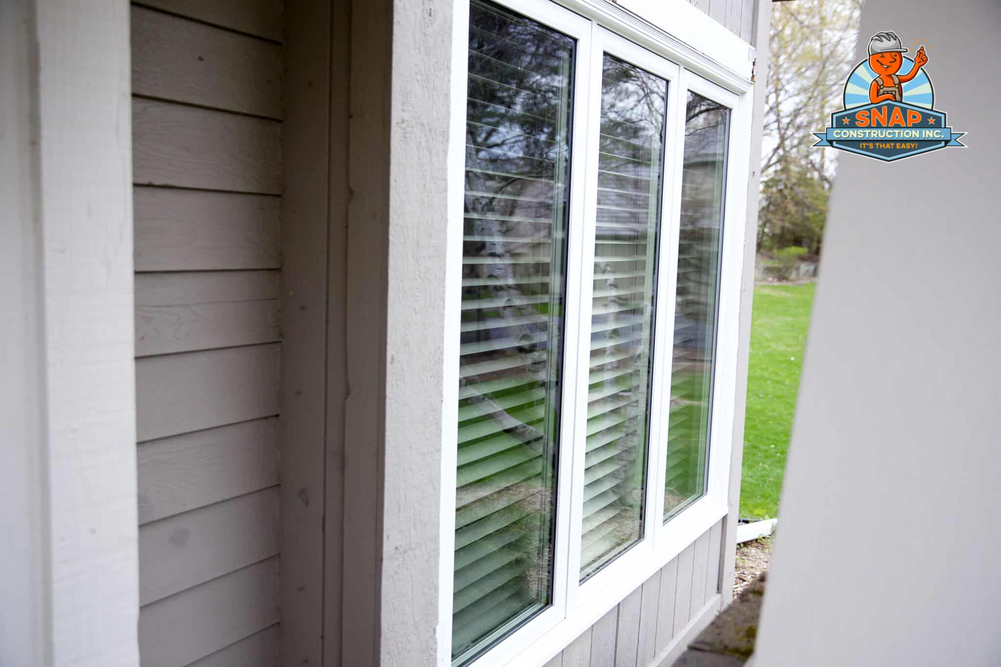 Snap Construction window installation on a gray-sided home in Bloomington MN featuring white-framed windows with blinds and lawn reflections